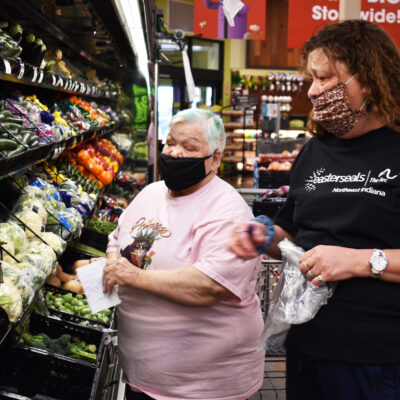 Two women select produce at a grocery store