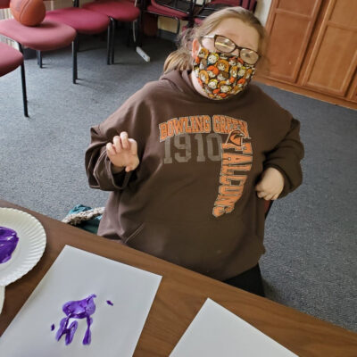 A young woman in face mask makes a painted hand print