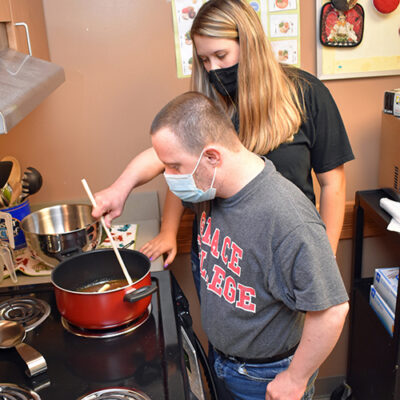 A woman watches a man stir a pot on a stove