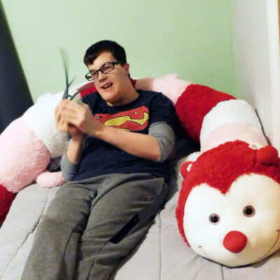 A young man lounges on a bed with a giant stuffed caterpillar