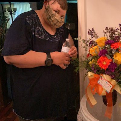 A woman stands near a vase of flowers