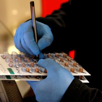 Close-up of gloved hand pushing a pill out of blister pack