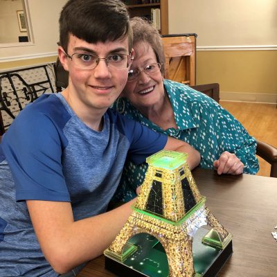 A young man and a senior woman smile together with a model of the Eiffel Tower