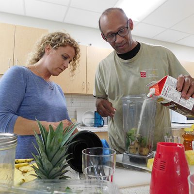 A woman watches a man pour liquid into a blender