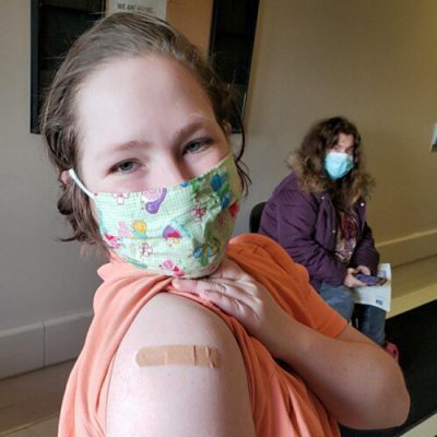 A young woman shows off a bandage on her arm after a shot