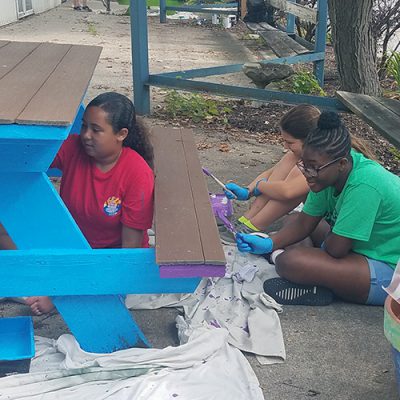 Three girls paint a picnic table