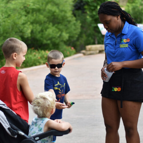A young woman working at the zoo, talks with a group of children.