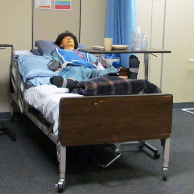 A manikin lies in a bed in a mock hospital room